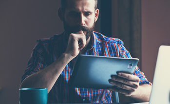 concentrated bearded man sitting with digital tablet and cup of coffee