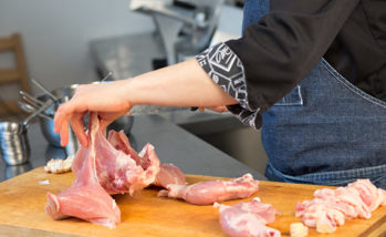 A person cuts raw chicken. Cook's hand with a knife close-up on